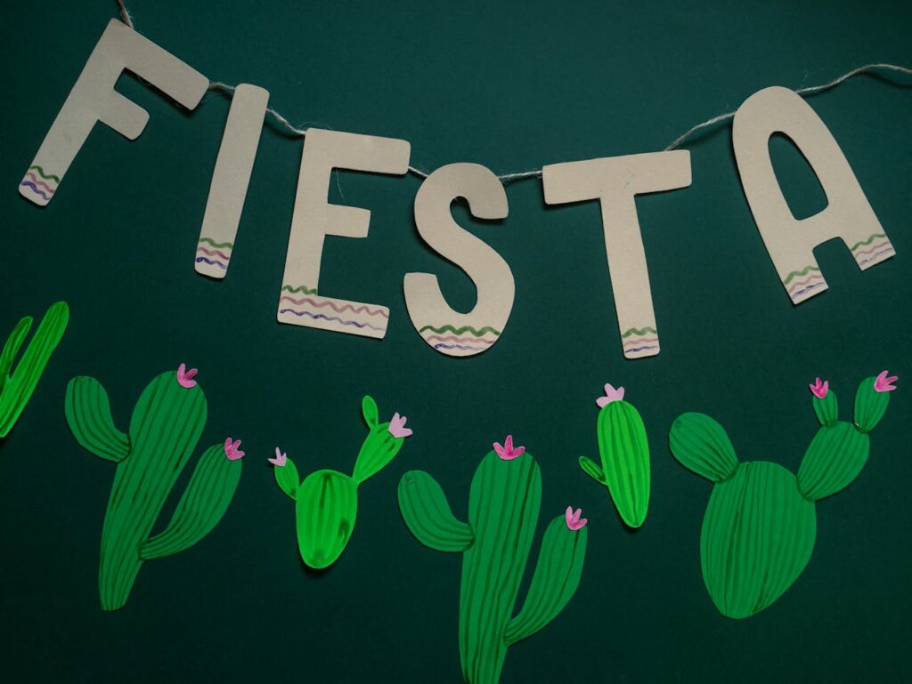 Vibrant fiesta-themed banner with paper cut-out cacti on a green background.